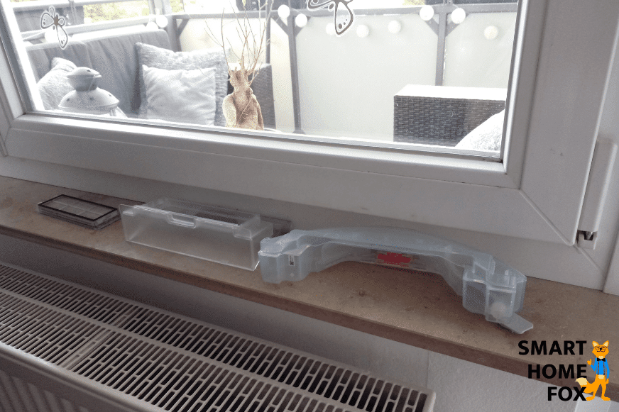 Пылесборник робота-пылесоса сушится на подоконнике после мытья